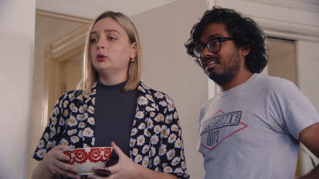 Two individuals standing in a hallway with a surprised expression, one holding a bowl.