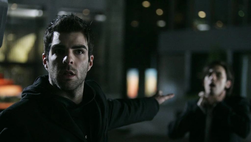 Two men outdoors at night, one in foreground looking surprised and the other in the background with an open mouth, possibly shouting.