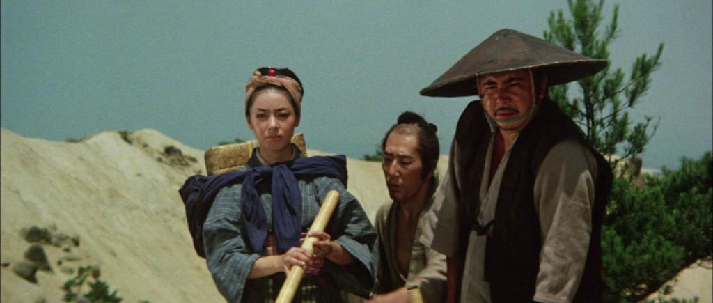 Three actors in traditional asian attire in a desert setting, portraying characters on a journey.