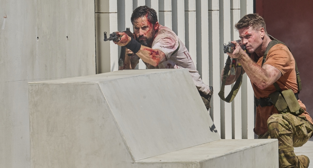 Two men in tactical gear aiming firearms from behind cover.