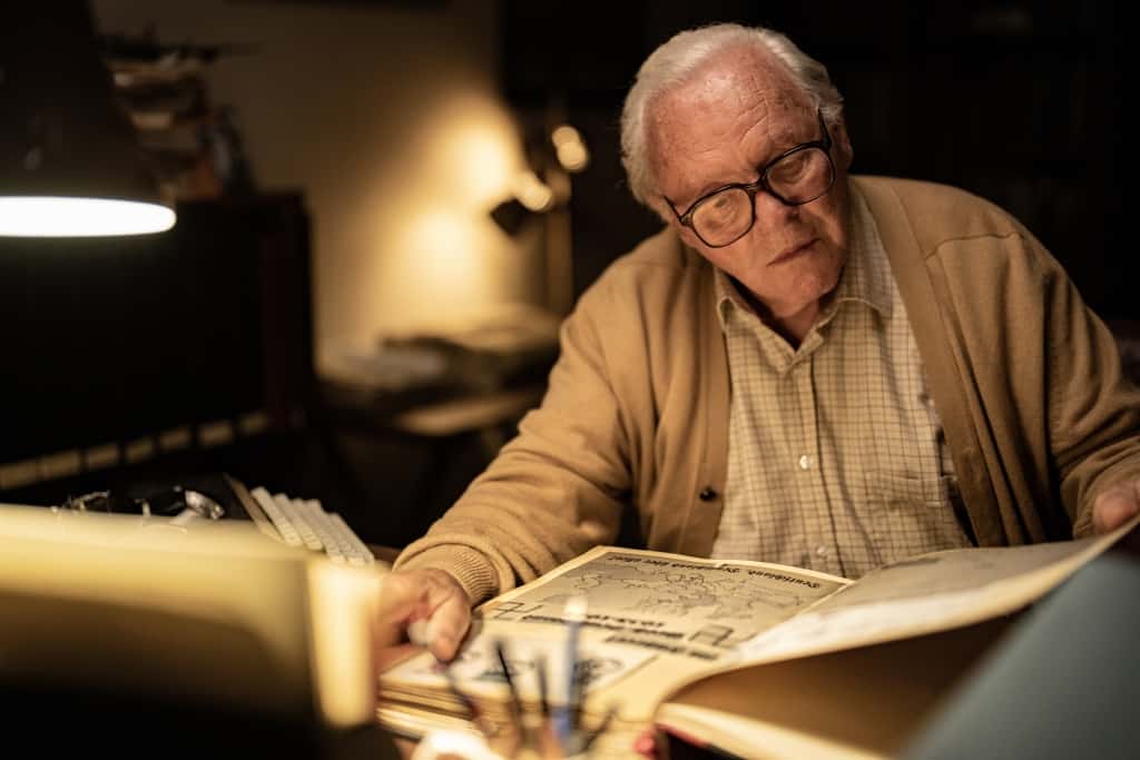 Senior man perusing documents at a desk with a lamp in a dimly lit room.
