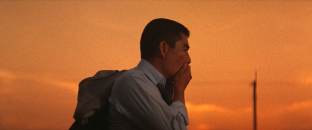 Profile of a contemplative man against an orange-hued sunset sky.