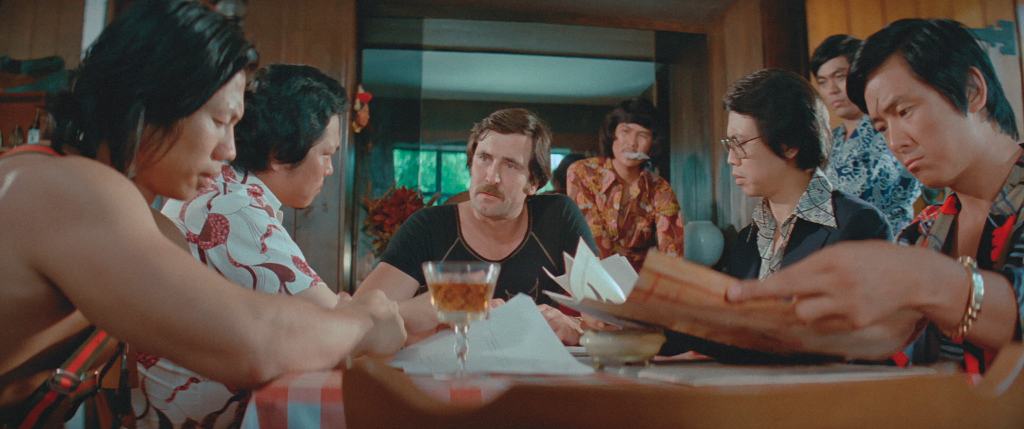 A group of people engaged in a tense conversation around a table, with one man in the center looking particularly serious.