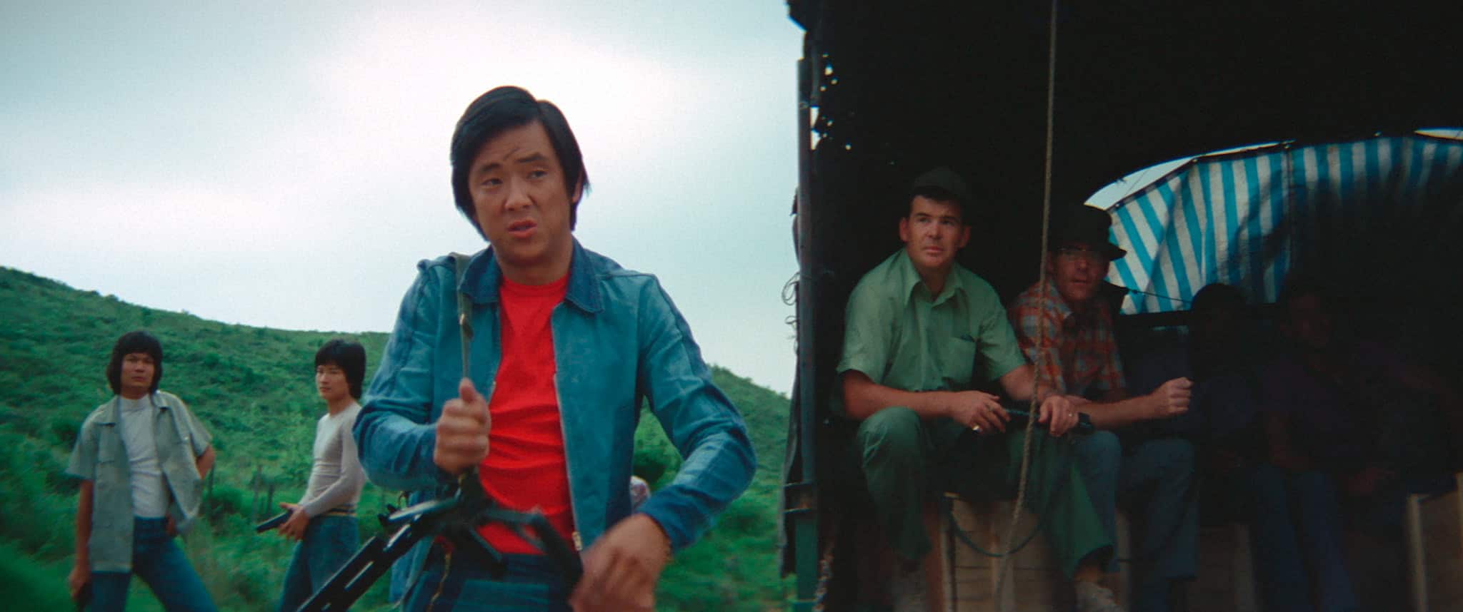Group of individuals with varied attire next to a train, one person at the forefront riding a bicycle.