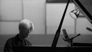 Janus Contemporaries To Release ‘Ryuichi Sakamoto | Opus’ On Blu-Ray This November Pianist focused on sheet music during a black and white performance scene.