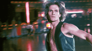 ‘Skatetown U.S.A.’ Blu-Ray Review – A ’70s Masterpiece On Wheels A man with long hair and a sleeveless top appears in motion against a blurred background featuring neon lights.