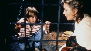 A boy and a woman talking through bars with concerned expressions.
