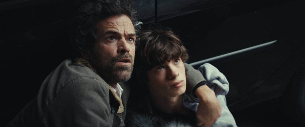 Two individuals, an adult and a teenager, looking intently in the same direction with expressions of concern or curiosity.