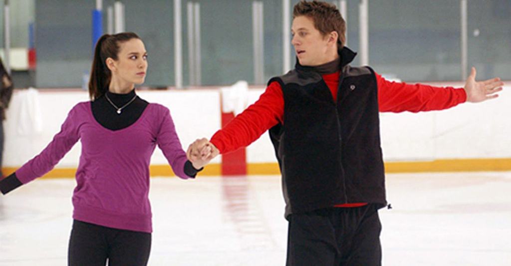 Two ice skaters practicing a routine on an indoor rink.