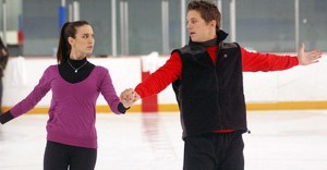 Two ice skaters practicing a routine on an indoor rink.