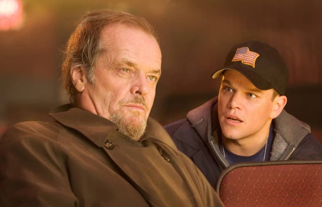 Two men focused on something out of frame, one older with a thoughtful expression, the other younger wearing a cap with an american flag patch.