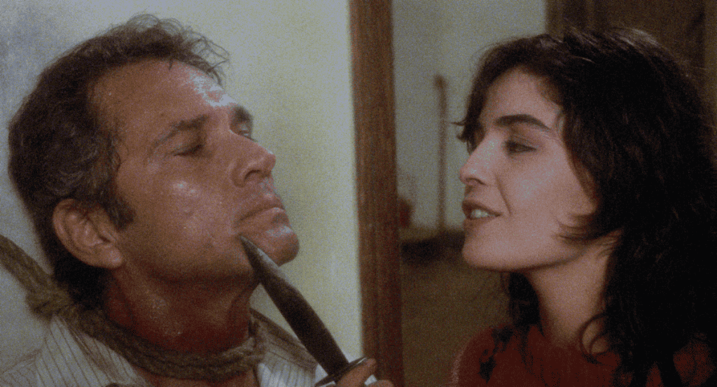 A woman holding a razor to a man's throat in a tense scene.