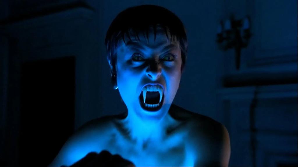 A person with a vampiric appearance displaying fangs in a dimly lit room.