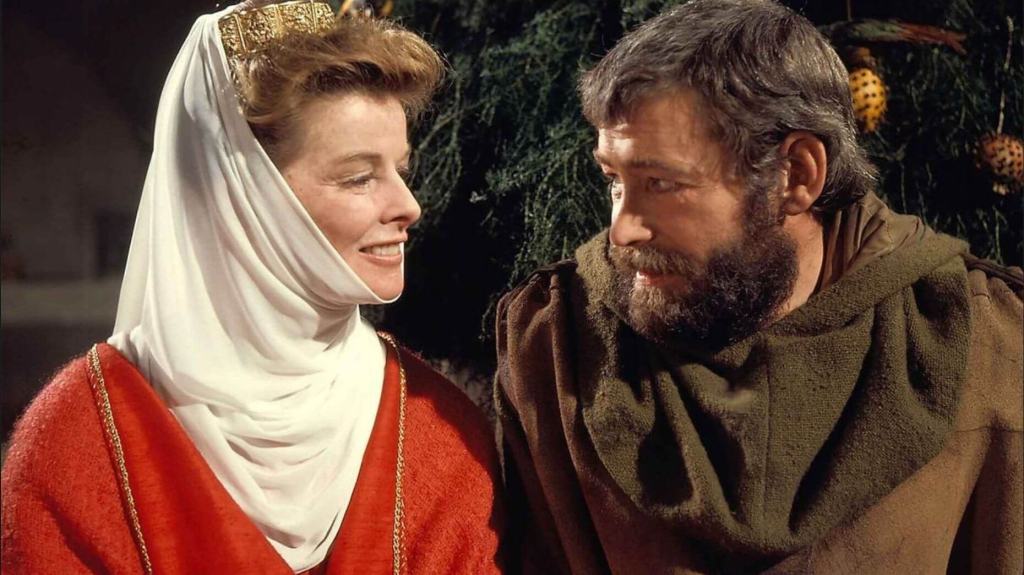 A man in medieval costume looks towards a smiling woman dressed as royalty.