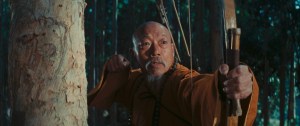 A focused archer in traditional attire drawing a bow amidst bamboo trees.
