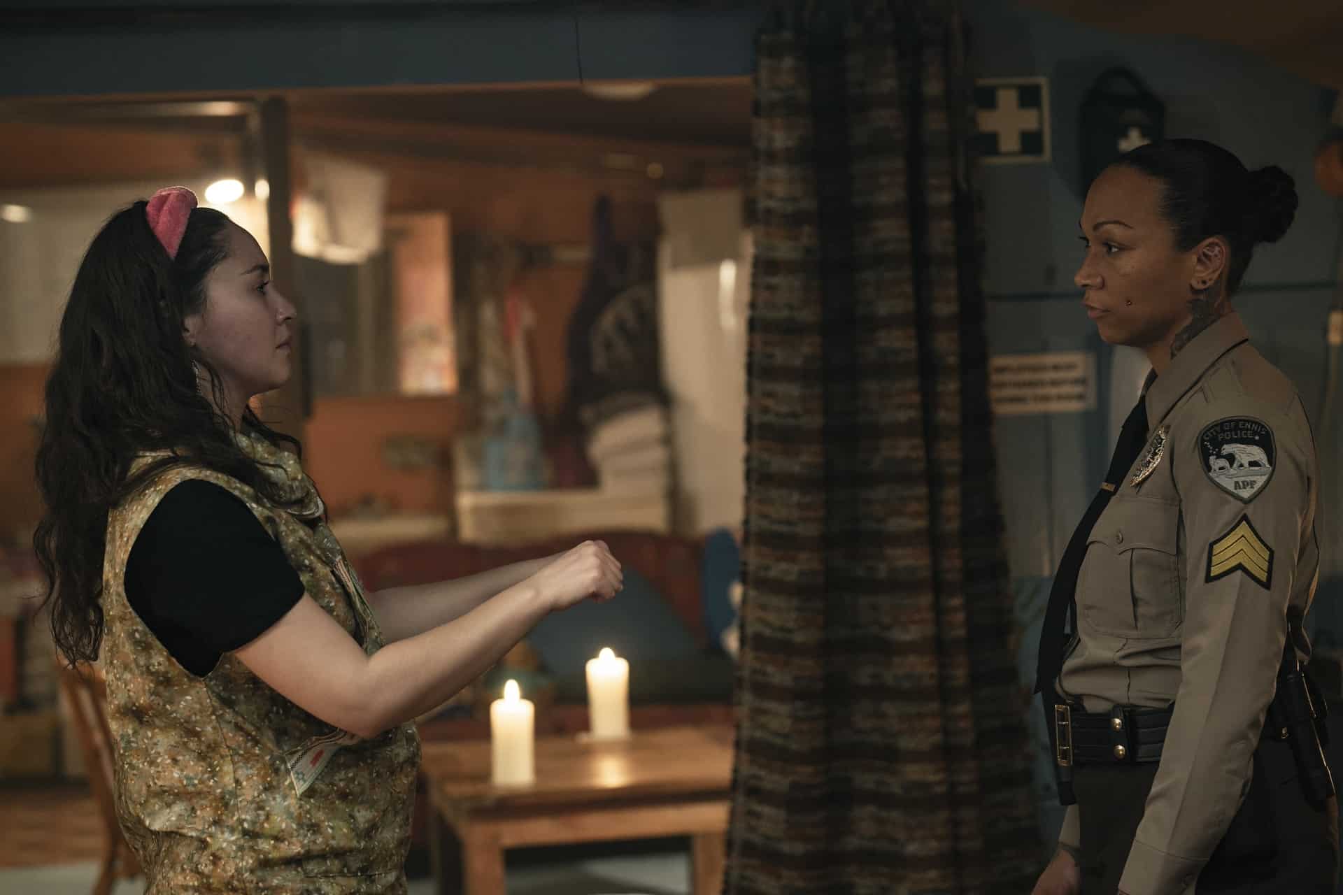 Two women in a dimly lit room, one in a sheriff's uniform and the other wearing a vest, appear to be having a serious conversation.