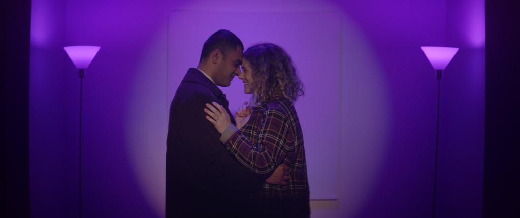 A couple sharing an intimate dance in a room illuminated by purple-tinted lights.