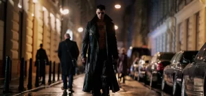 A person walking confidently down a city street at night, illuminated by street lights and surrounded by parked cars.