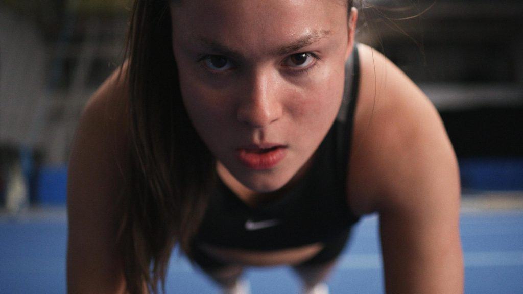 A young woman is doing push ups on a blue field.