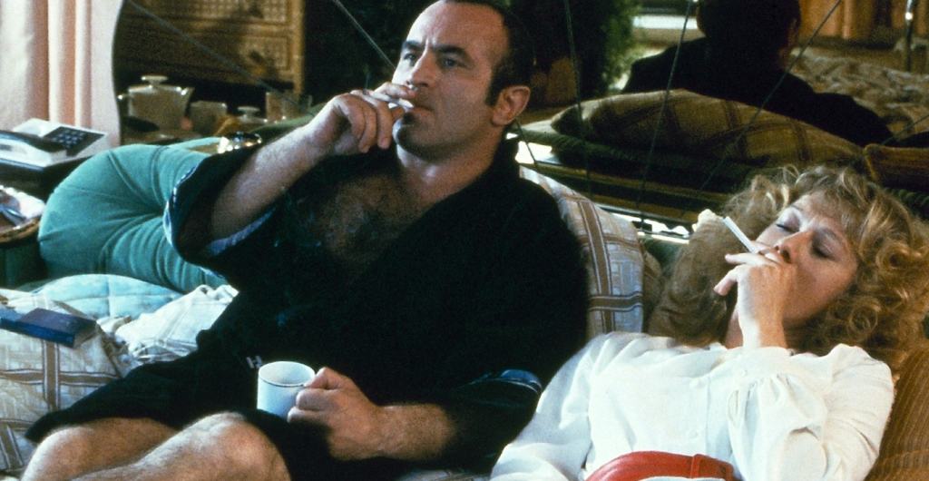 A man and a woman lounging on a couch, both smoking and looking thoughtful.