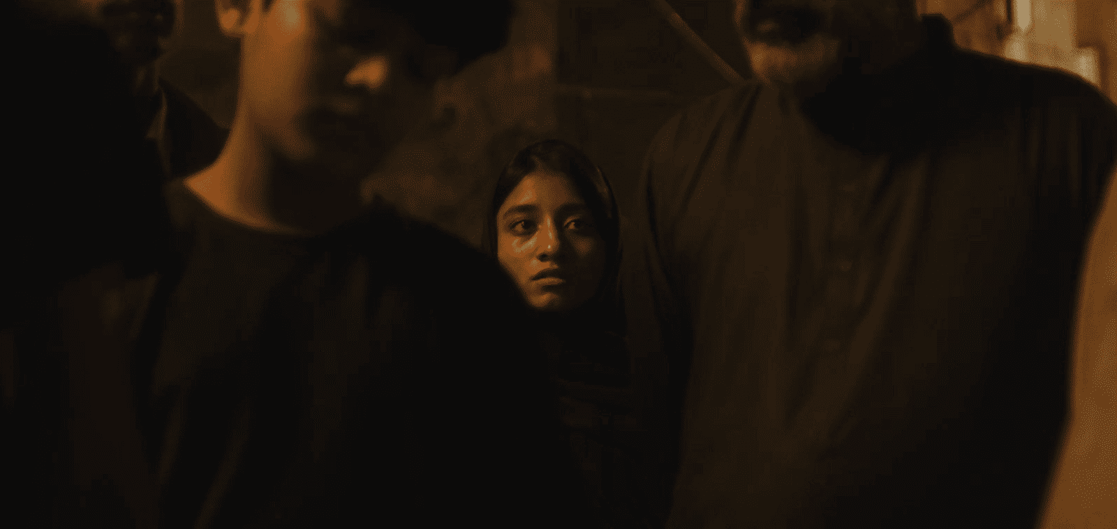A young woman looking anxious among a group of people in a dimly lit setting.