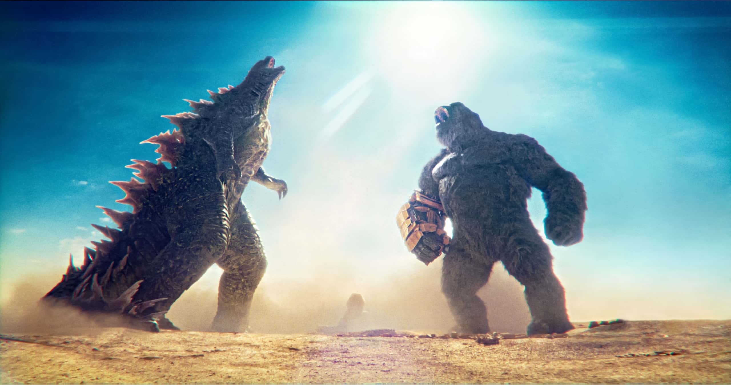 Two colossal monsters facing off under a bright sun with a dusty atmosphere around them.