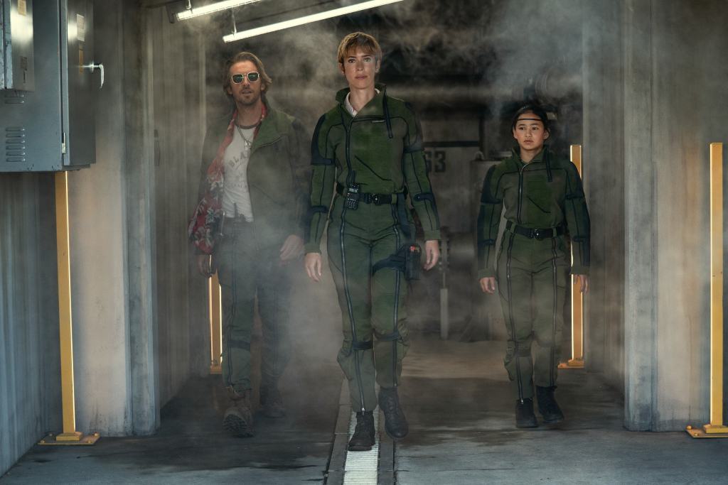 Three people in military uniforms walking through a smoky corridor with a determined look.
