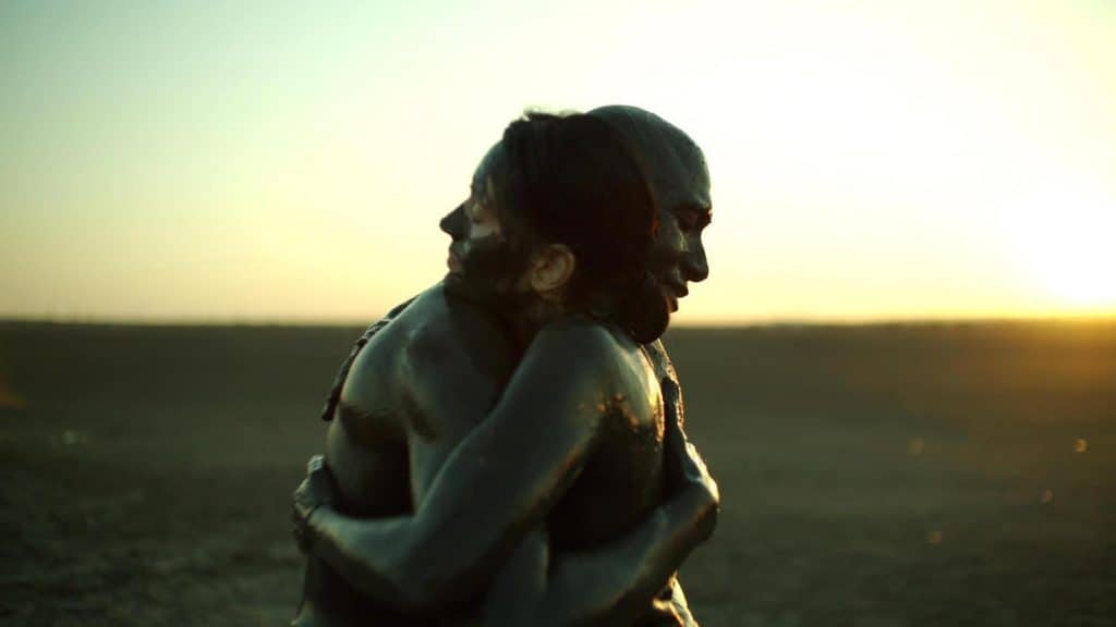 Two people hugging in the middle of a field at sunset.