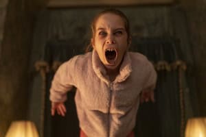 Young girl wearing a robe screams dramatically, lit from below, with dark curtains and lamps in the background.