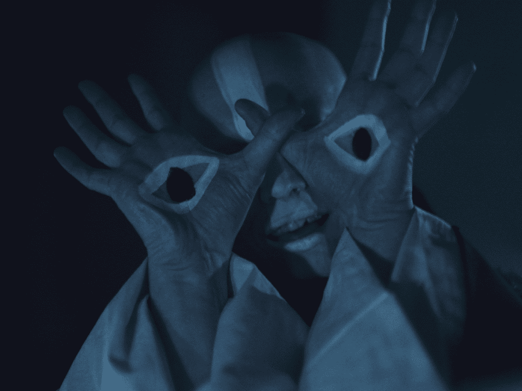 A person with painted facial features on their hands covering their face, creating a surreal optical illusion.