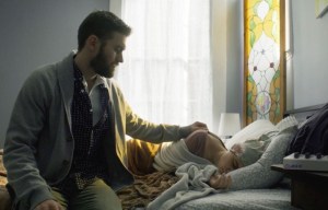 ‘Bag Of Lies’ Blu-Ray Review – How Far Would You Go To Save A Loved One? A man seated beside a bed, looking at a young child sleeping under a blanket, in a room with a stained glass window.