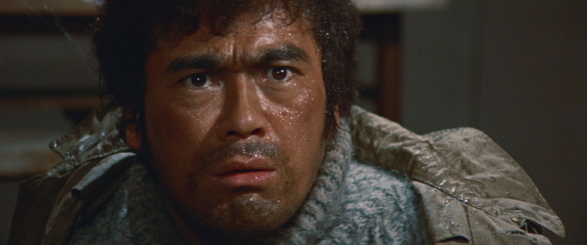 Close-up of a distressed man with sweat on his face, wearing a dirty, frost-covered jacket, looking intently to the side.