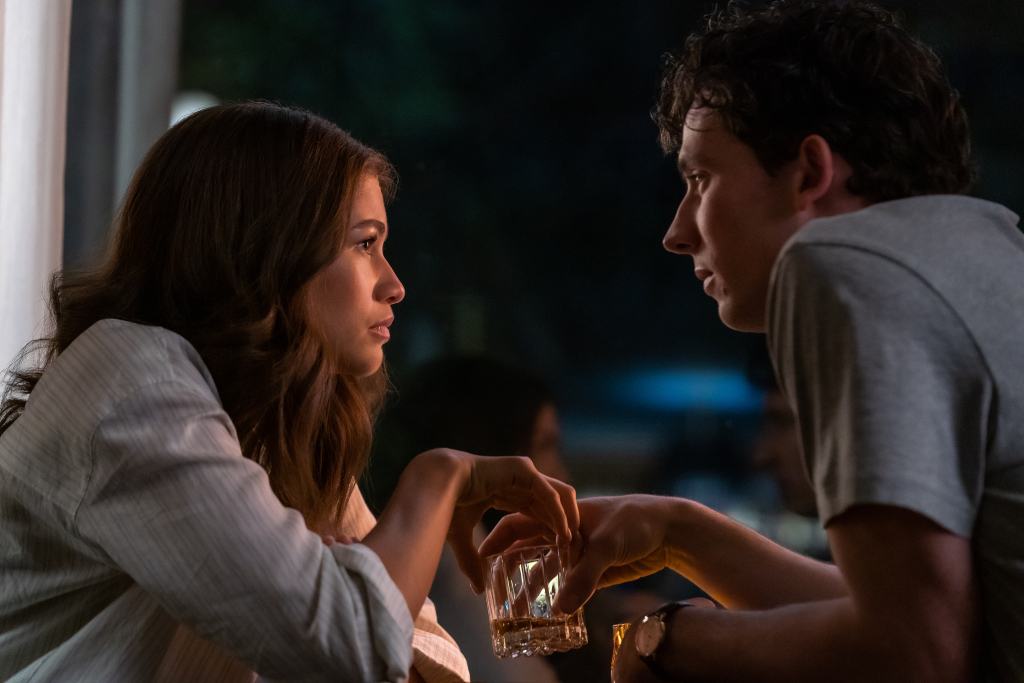 A man and a woman with a drink between them, engaged in a serious conversation at night.