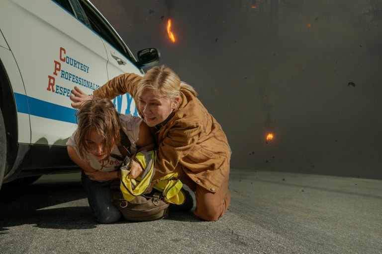Two individuals crouching behind a car for safety amidst an apparent dangerous situation with debris falling around them.