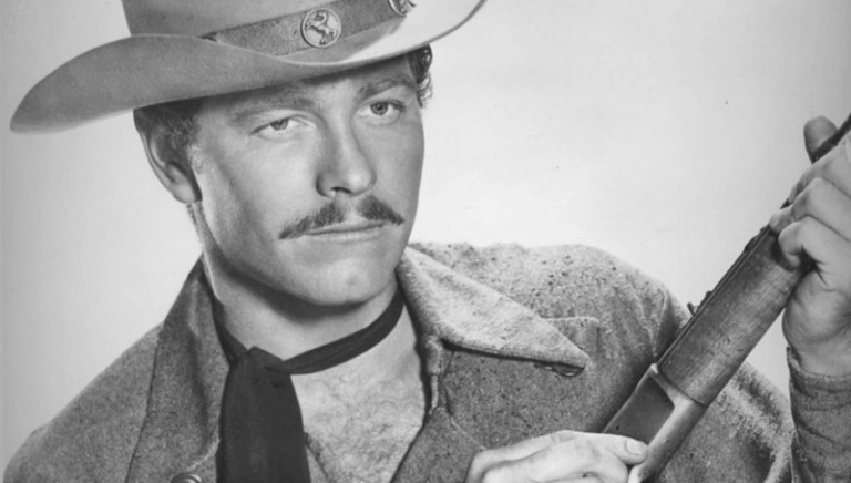 Black and white photo of a man in a cowboy hat, holding a rifle, with a mustache, looking to the side.