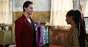 ‘Daniel Isn’t Real’ Blu-Ray Review – Imaginary Friends Are Meant To Be Forgotten A man in a red blazer smiling at a woman with braided hair in a striped top, standing in a room with a rustic interior.
