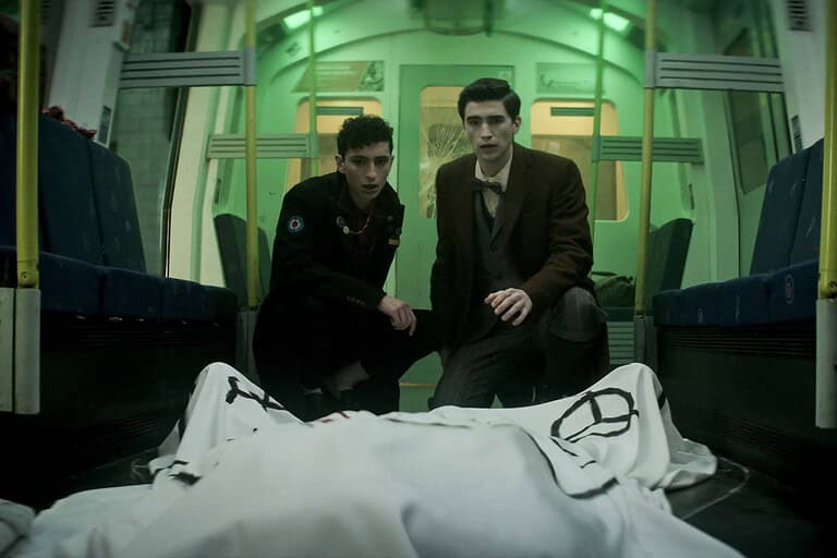 ‘Dead Boy Detectives’ Season 1 Review- A Hauntingly Entertaining Addition To Netflix’s Sandman Universe Two young men in a subway car, looking intently at a covered body lying on the floor between them.