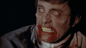A close-up of a man with a pale, ghoulish complexion and blood around his mouth, displaying an intense, fearful expression.