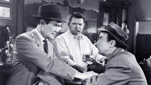 Film Noir: The Dark Side Of Cinema XVIII Blu-Ray Review – A Gritty Trio Of Deception & Murder Three men in a vintage setting, with one holding a drink and engaging in a serious conversation.
