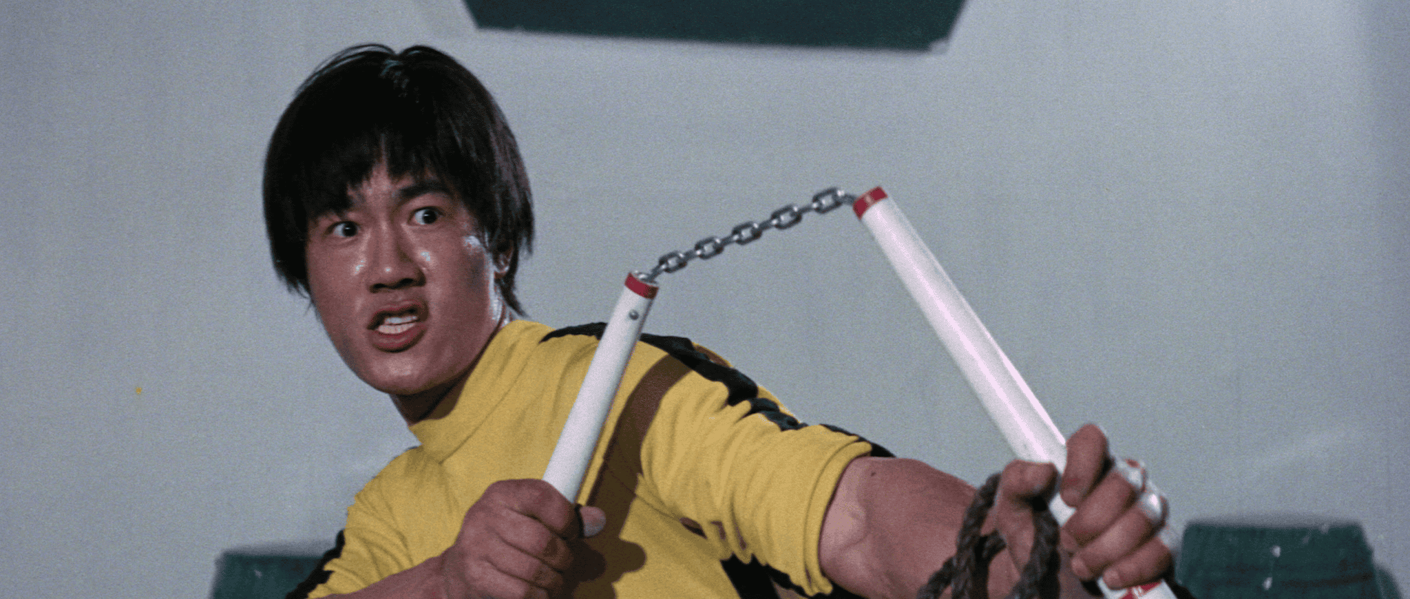Man in yellow top wielding nunchaku with intense expression.