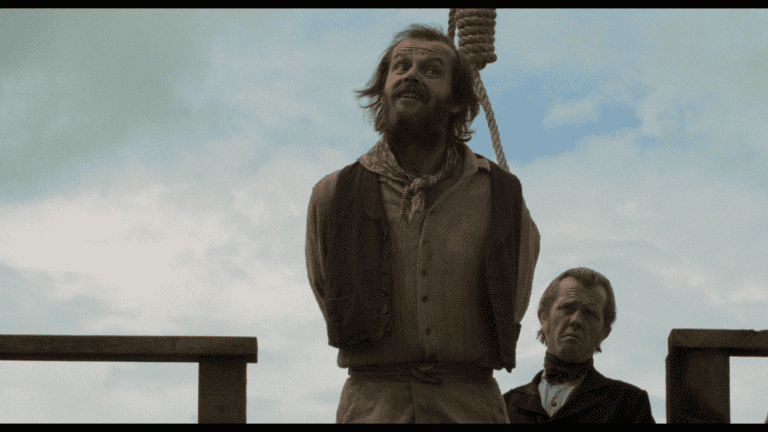 A man with a noose around his neck stands next to another man, both on a wooden platform, with the sky in the background.