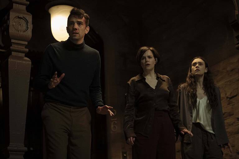 ‘Humane’ Review – Caitlin Cronenberg’s Debut Feature Lacks Bite Three people look anxious in a dimly lit room, with an old clock in the background showing 12:06.