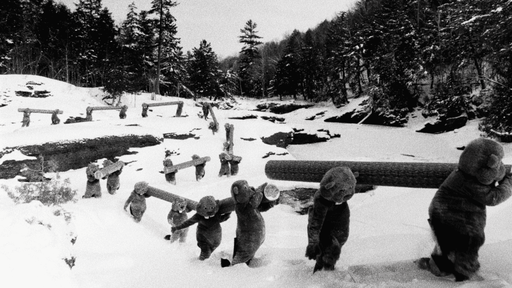 A snowy landscape with a line of carved wooden bear statues, each holding a log, amid snow-covered trees and terrain.
