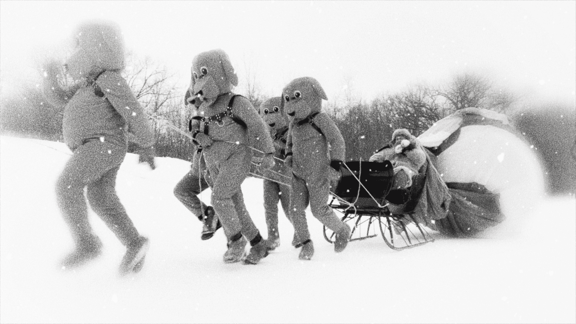 Black and white image of individuals in vintage deep-sea diving suits pulling a sled through a snowy landscape.