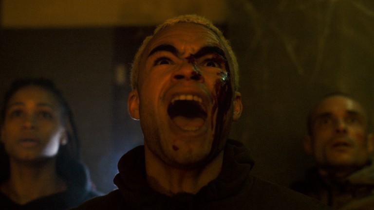 A man screaming with blood on his face, flanked by two other concerned individuals.