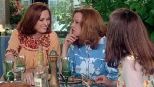 Jeanne Moreau: Filmmaker Blu-Ray Review – Three Overlooked Gems From A French Icon Two women seated at a dining table, one whispering to the other, surrounded by food and drinks, in a lively, floral-decorated setting.