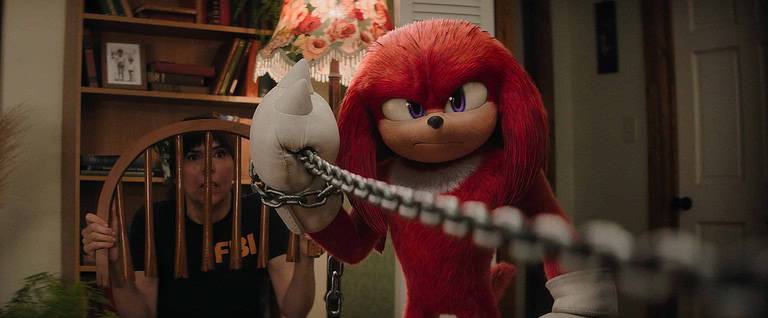 A woman in an fbi vest looks surprised next to a large, animated red echidna character holding a hand in chains.