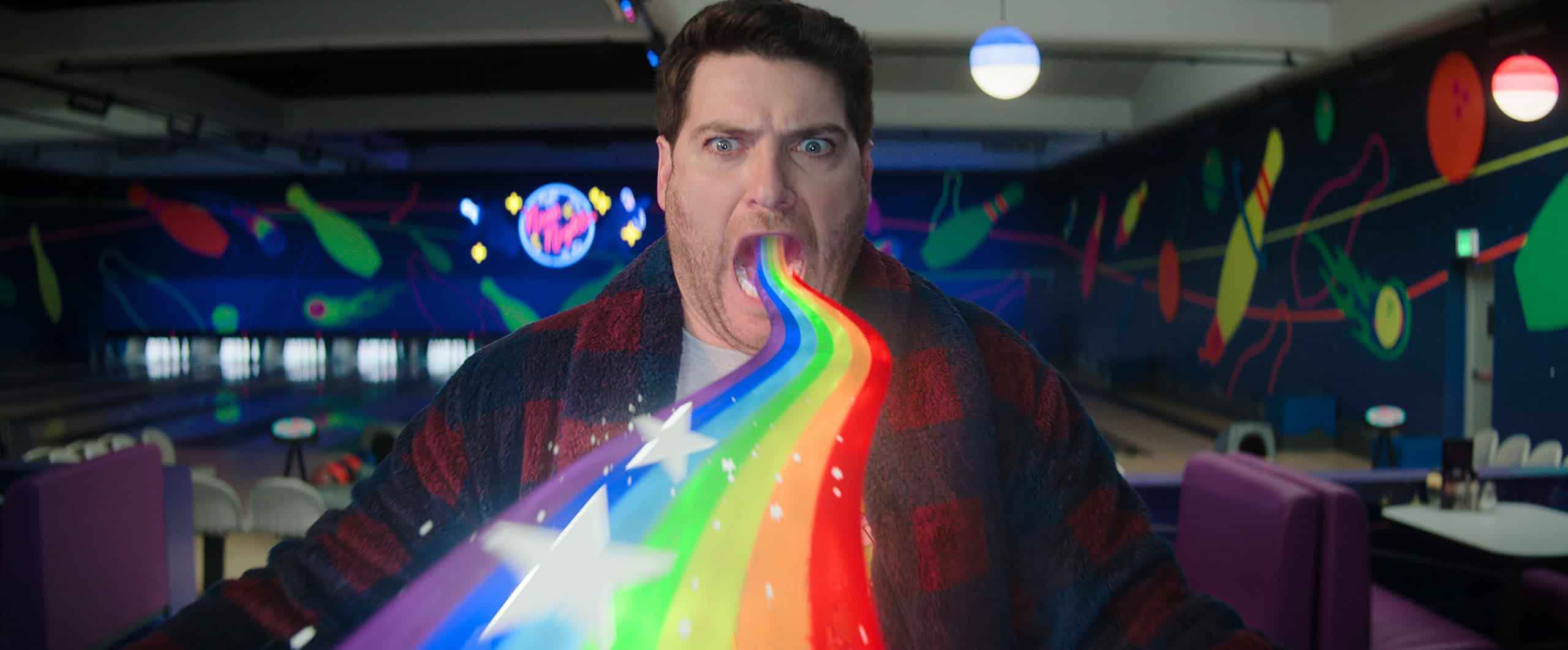 Man in a bowling alley with a colorful rainbow stream and stars flowing out of his open mouth, expressing surprise or excitement.