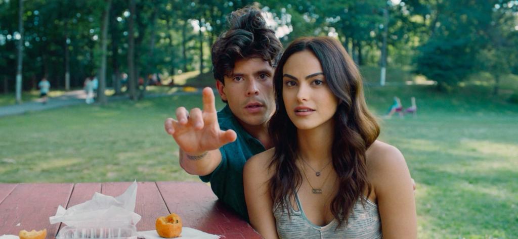 Two individuals sitting at a picnic table in a park, with one of them pointing at something in the distance.