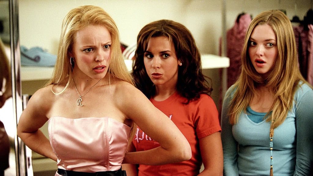 Three young women in a clothing store, looking surprised and slightly displeased; two are blonde and one is brunette.